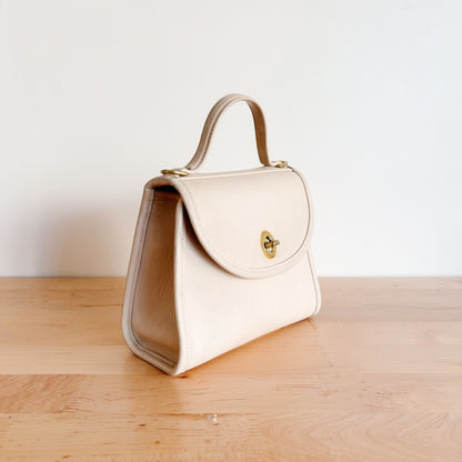 Vintage Coach Regina bone handbag with a gold clasp on a wooden surface