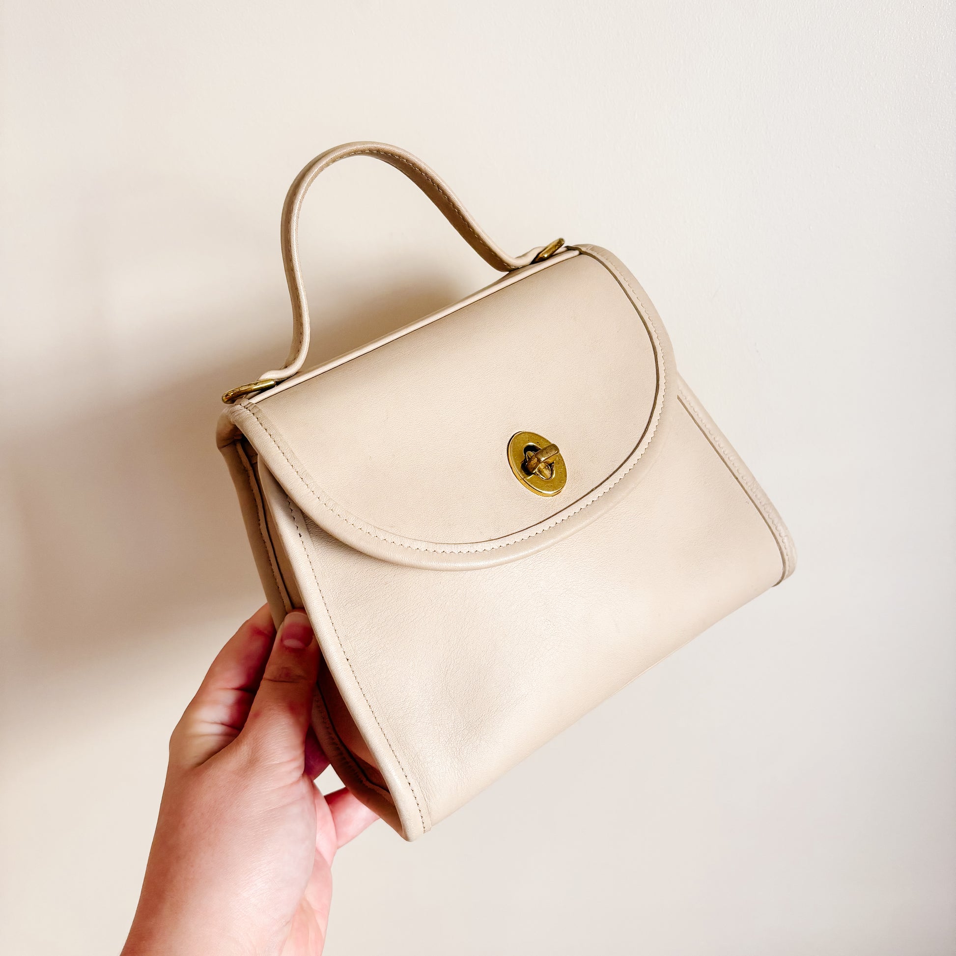 Vintage Coach Regina bone colour handbag held by a hand against a plain background